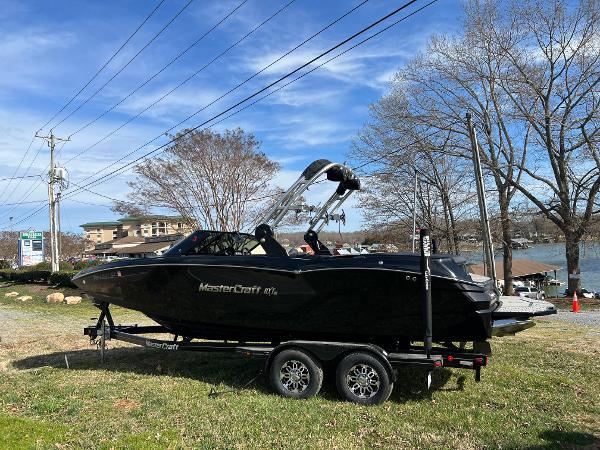 MasterCraft NXT22 2020 MasterCraft NXT22 boat on trailer, parked near a lake with clear blue sky.
