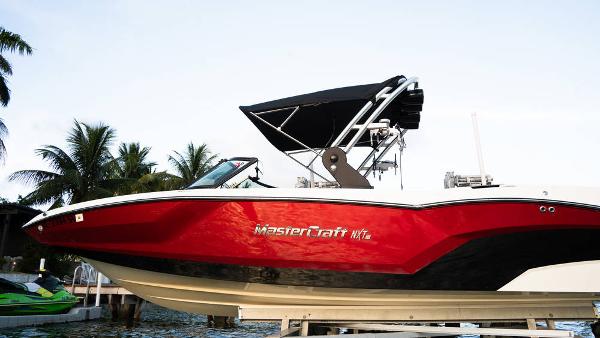 MasterCraft NXT24 2021 MasterCraft NXT24 boat with red hull, docked near palm trees.