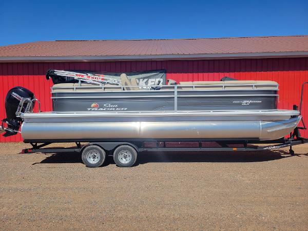 Sun Tracker Party Barge 24 DLX 2024 Sun Tracker Party Barge 24 DLX pontoon boat on trailer, red building background.