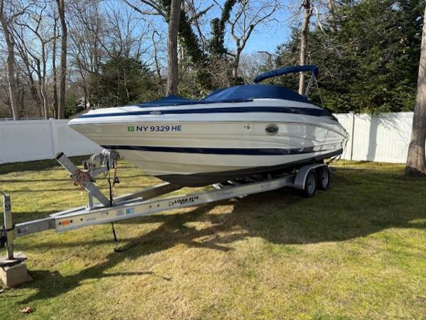 Crownline 270 SS 2016 Crownline 270 SS boat on trailer, parked on grass, surrounded by trees and a white fence.
