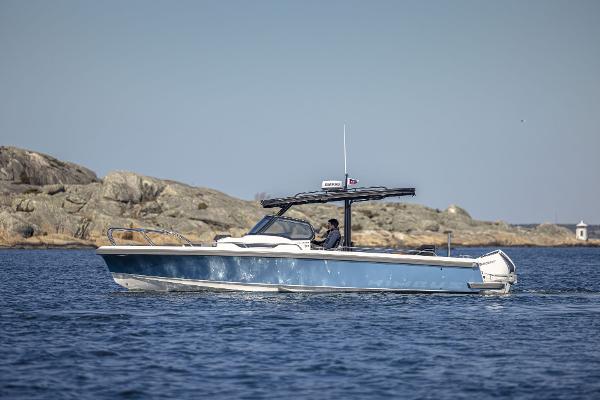 Nimbus T9 2024 Nimbus T9 boat cruising on a calm sea near rocky shore.