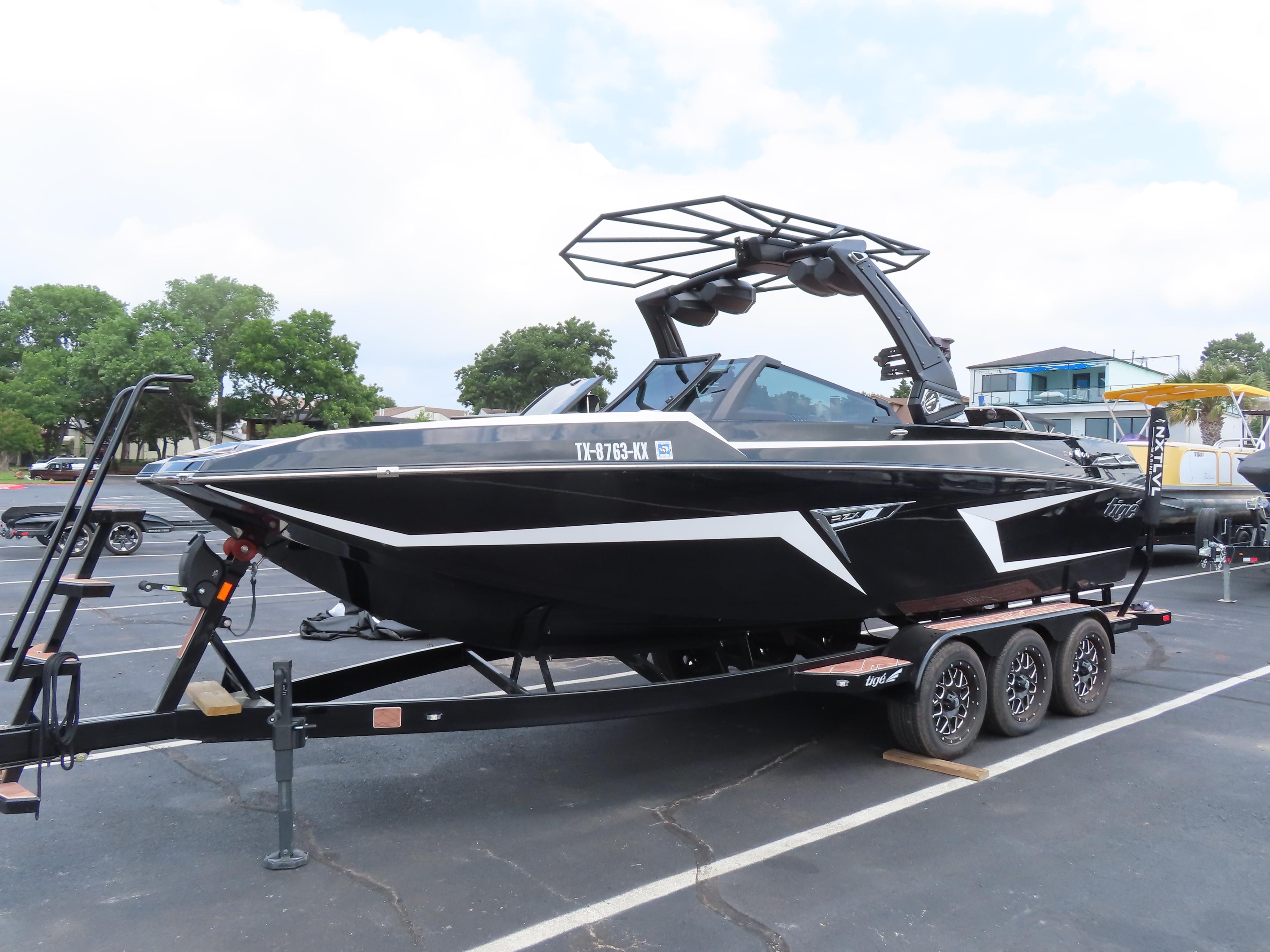 Tigé 24RZX 2023 Tigé 24RZX boat on trailer, black with white accents, parked outdoors.