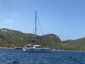 Lagoon 40 2019 Lagoon 40 catamaran sailing near rocky coastline under clear blue sky.