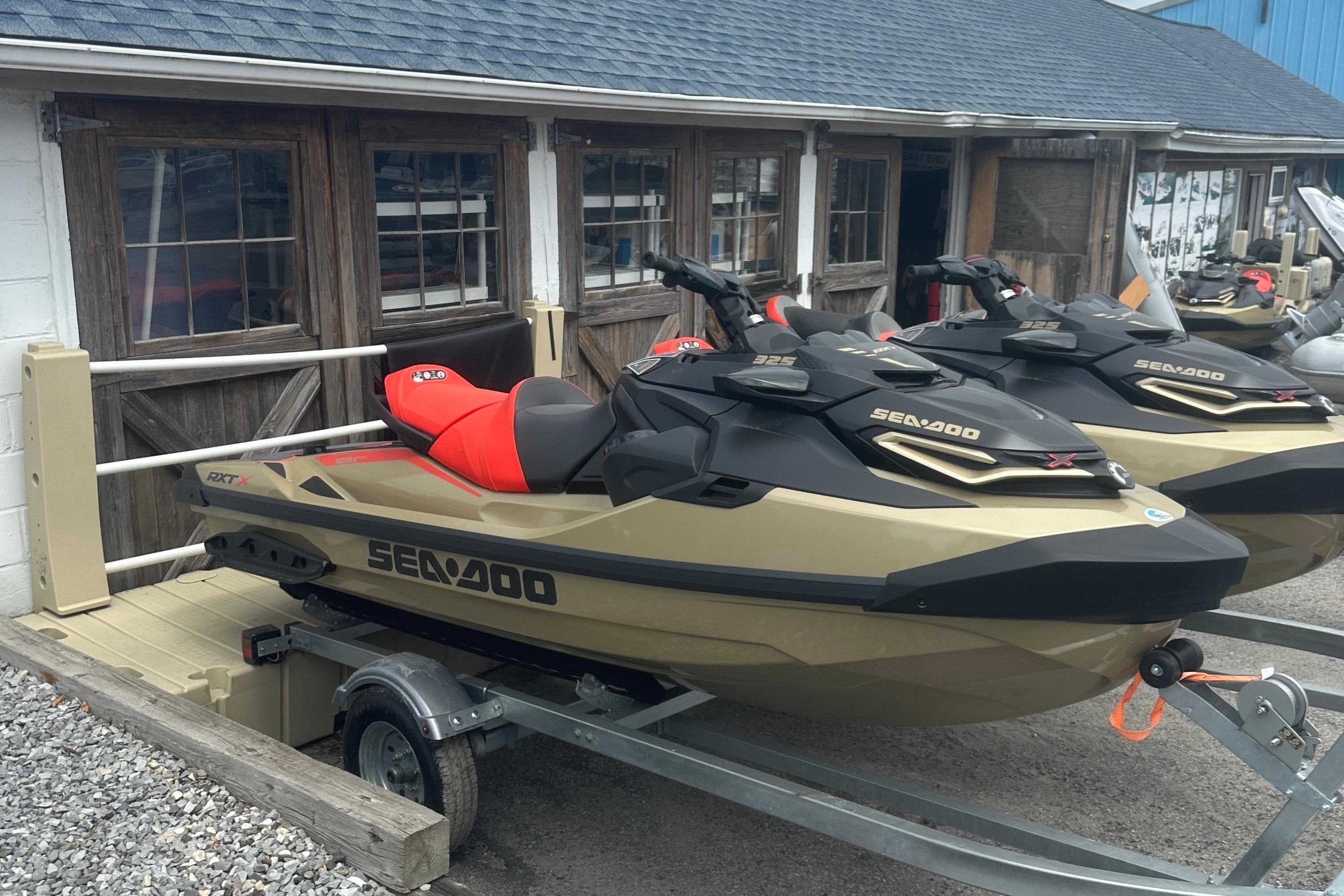 Sea-Doo RXT-X 325 2025 Sea-Doo RXT-X 325 jet ski on trailer, parked outside wooden building.