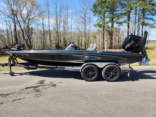 Triton 20XP Patriot 2024 Triton 20XP Patriot boat on trailer, parked on road with trees in background.