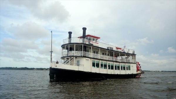 Custom Paddle Wheel Vintage 1984 custom paddle wheel boat cruising on a calm river under cloudy skies.
