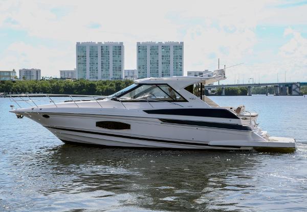 Regal 46 Sport Coupe 2016 Regal 46 Sport Coupe yacht cruising on a calm river with cityscape background.