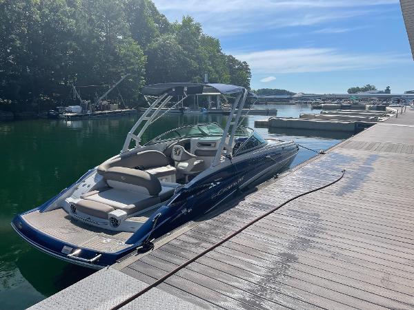 Crownline E255 2019 Crownline E255 boat docked at a serene marina with lush greenery.