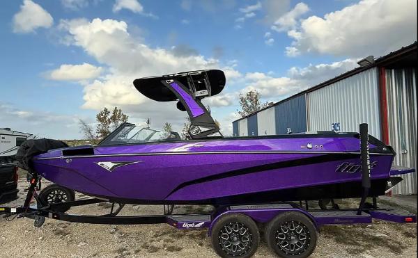 Tigé Z3 2022 Tigé Z3 boat in vibrant purple, parked on a trailer near a metal building.