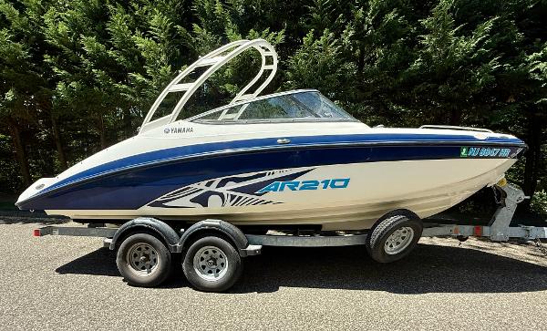 Yamaha Boats AR210 2022 Yamaha AR210 boat on trailer, parked outdoors, surrounded by trees.