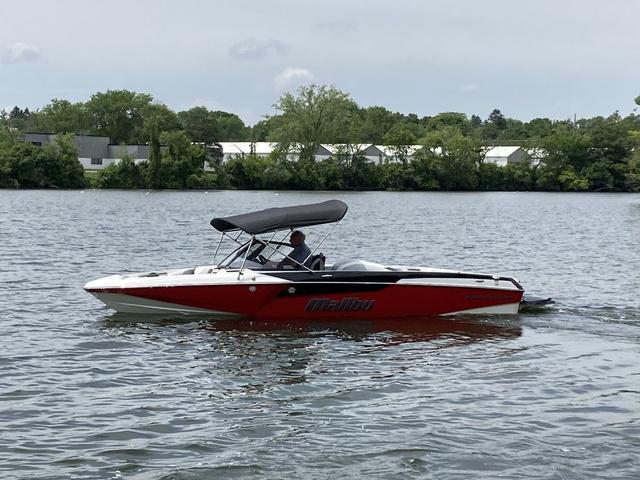 Malibu TXi Mo 2024 Malibu TXi Mo boat cruising on a calm lake with trees in the background.