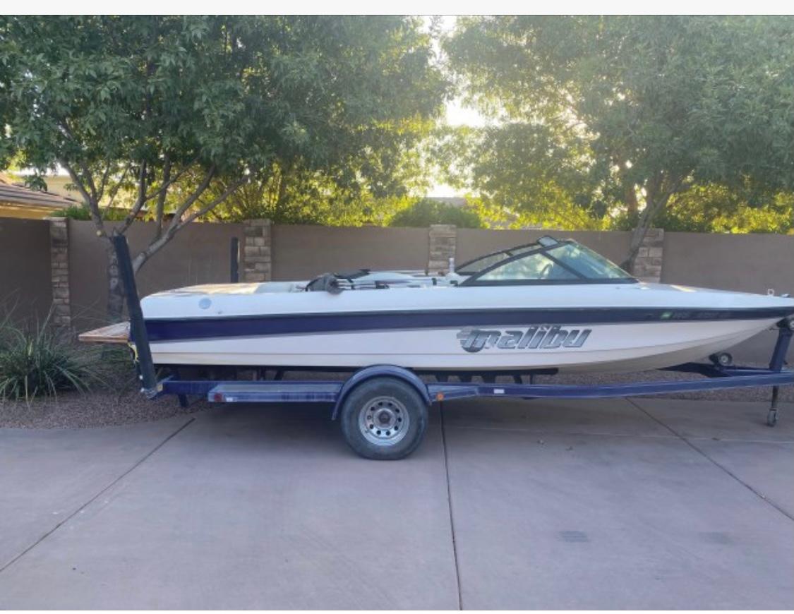 Malibu Response LX 1999 Malibu Response LX boat on trailer, parked outdoors with trees in the background.