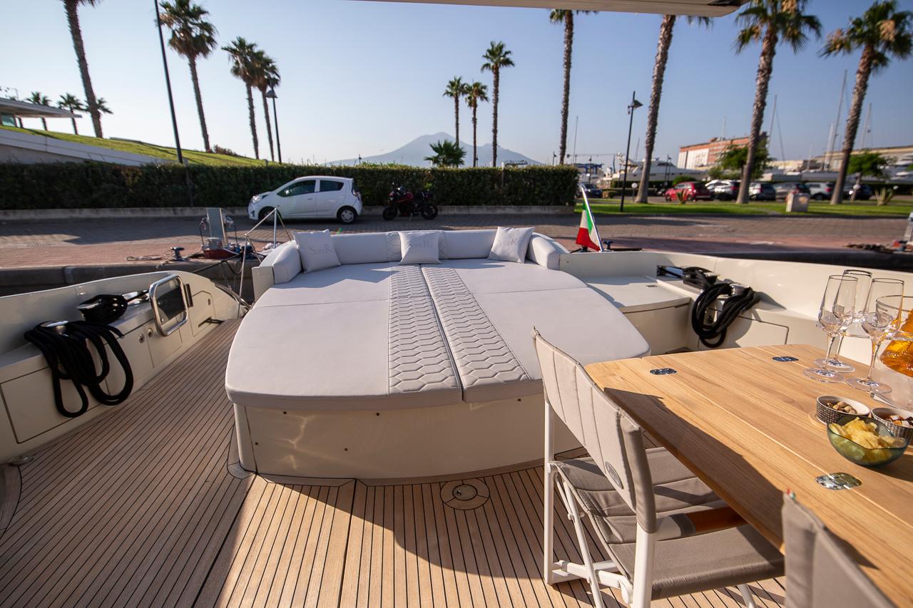 Azimut 68S Luxurious 2005 Azimut 68S yacht deck with sunbed, dining area, and scenic marina view.