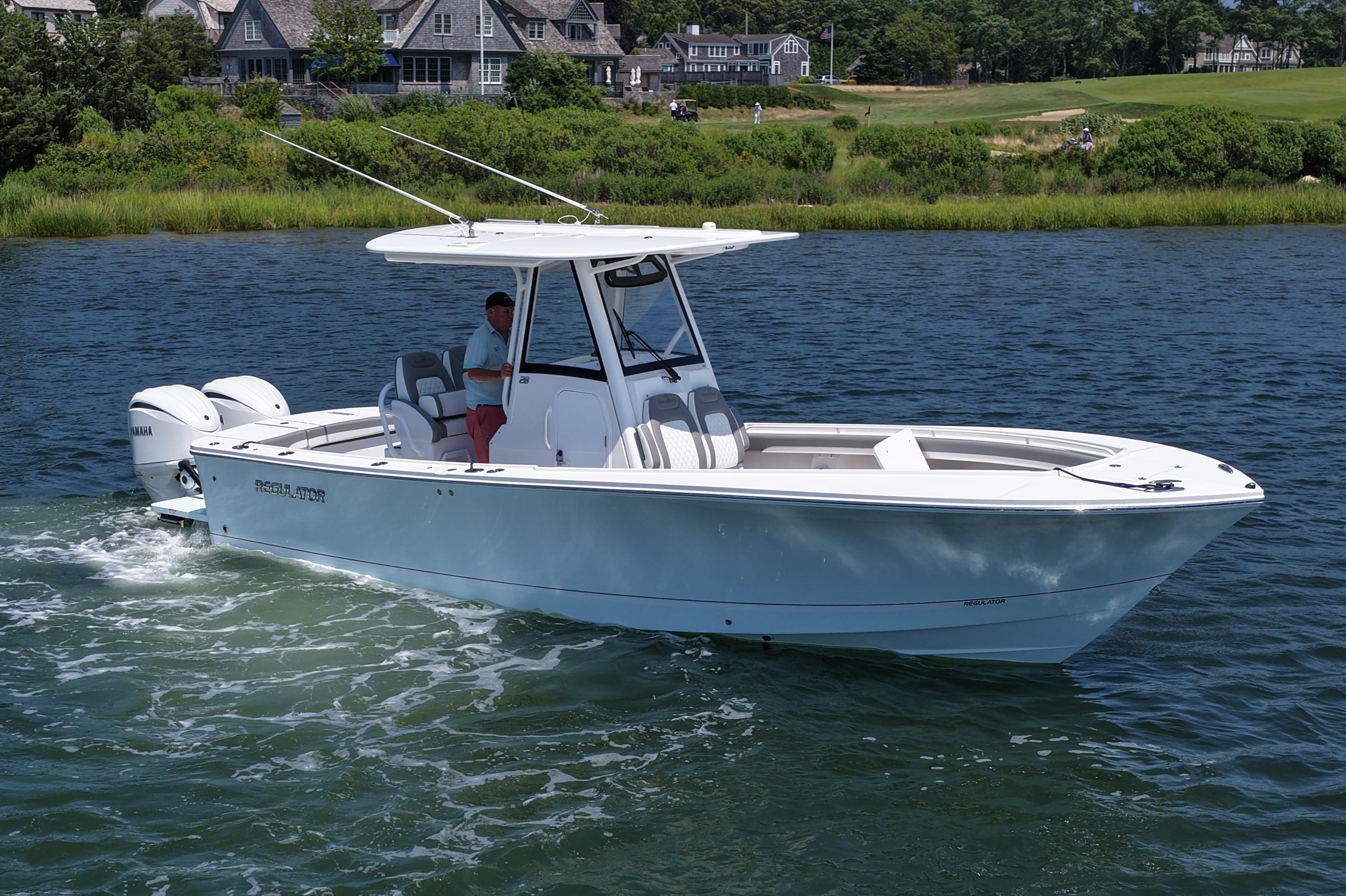 Regulator 28 2025 Regulator 28 boat cruising on a scenic waterway near lush greenery and houses.
