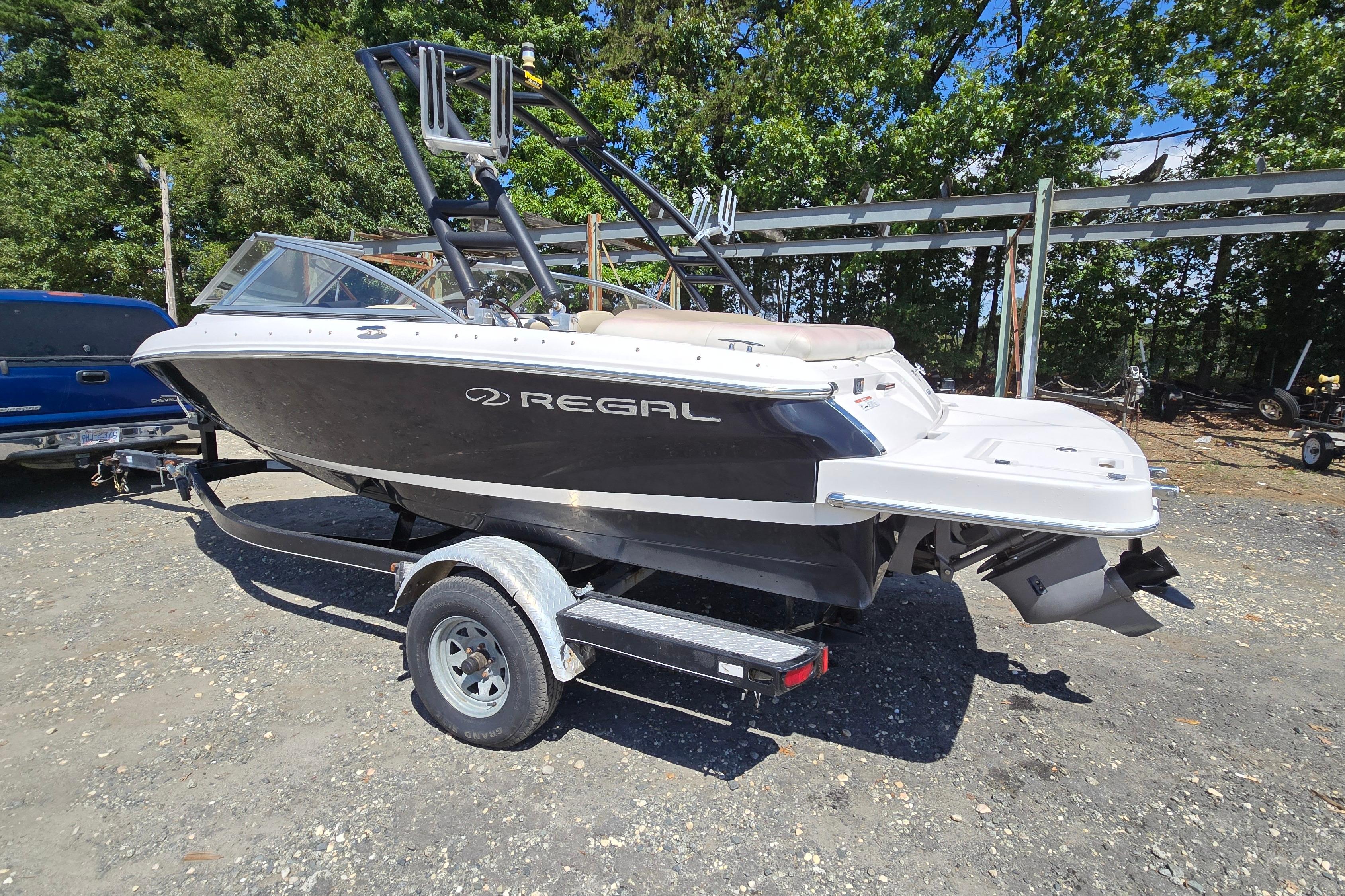 Regal 1900 Bowrider 2015 Regal 1900 Bowrider boat on trailer, parked outdoors, surrounded by trees.
