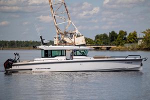 Axopar 37 XC CROSS CABIN 2024 Axopar 37 XC boat on calm water with industrial backdrop.