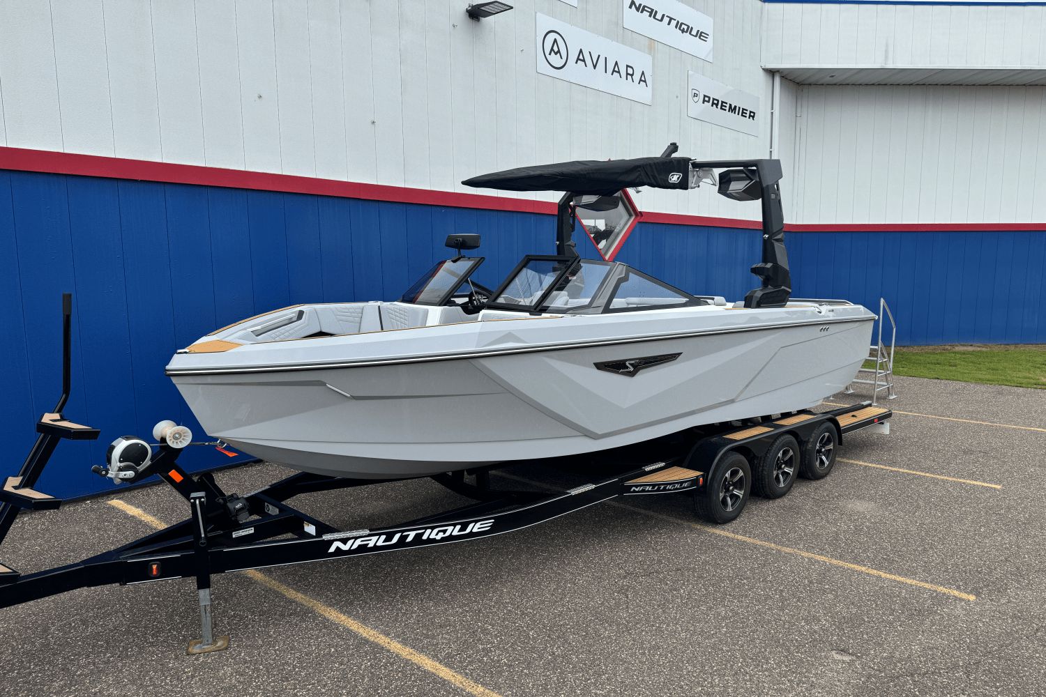 Nautique S23SUPER AIR 2026 Nautique S23 Super Air boat on trailer, parked outside dealership.