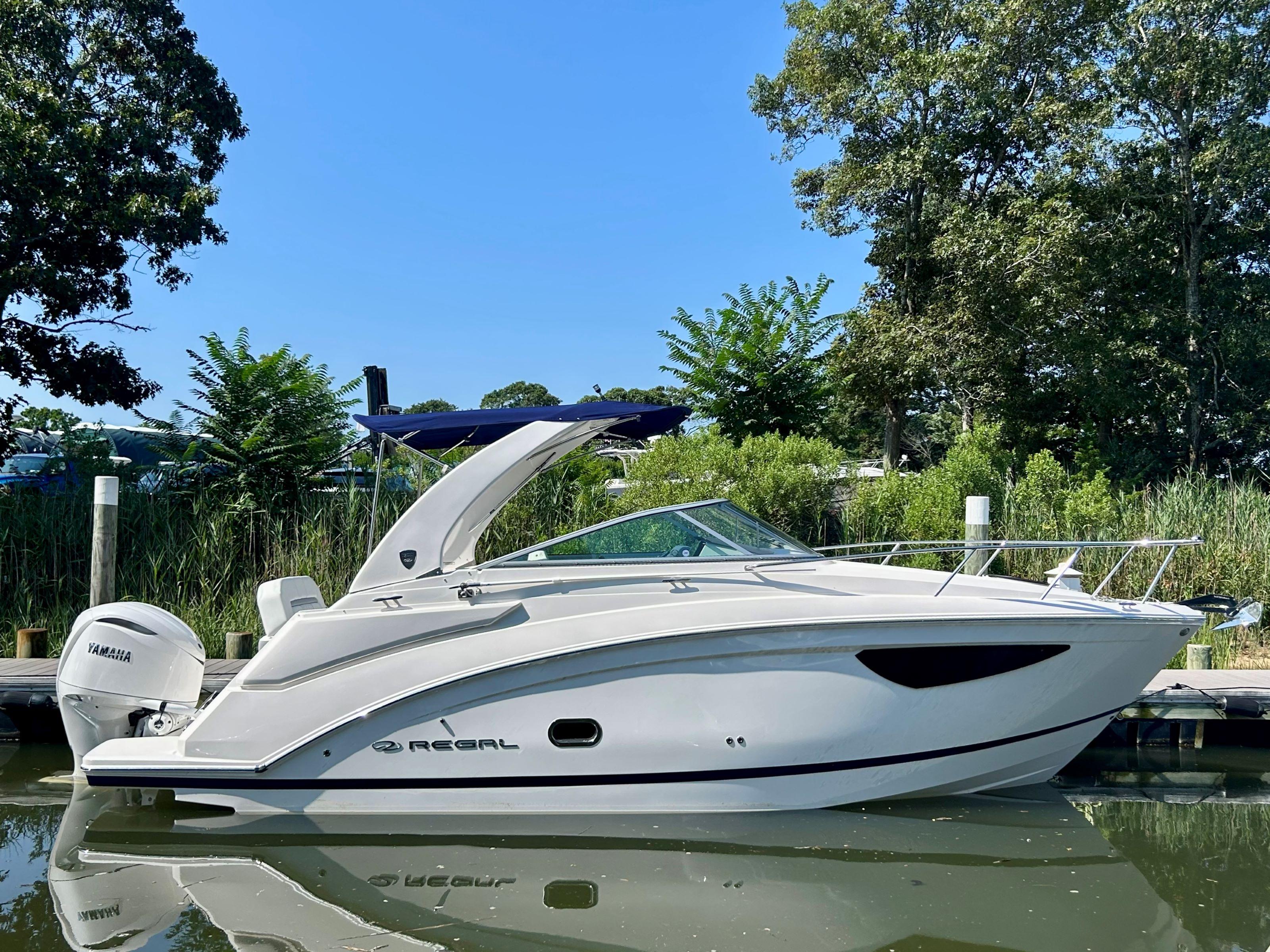 Regal 26 XO 2025 Regal 26 XO boat docked on calm water, surrounded by lush greenery.