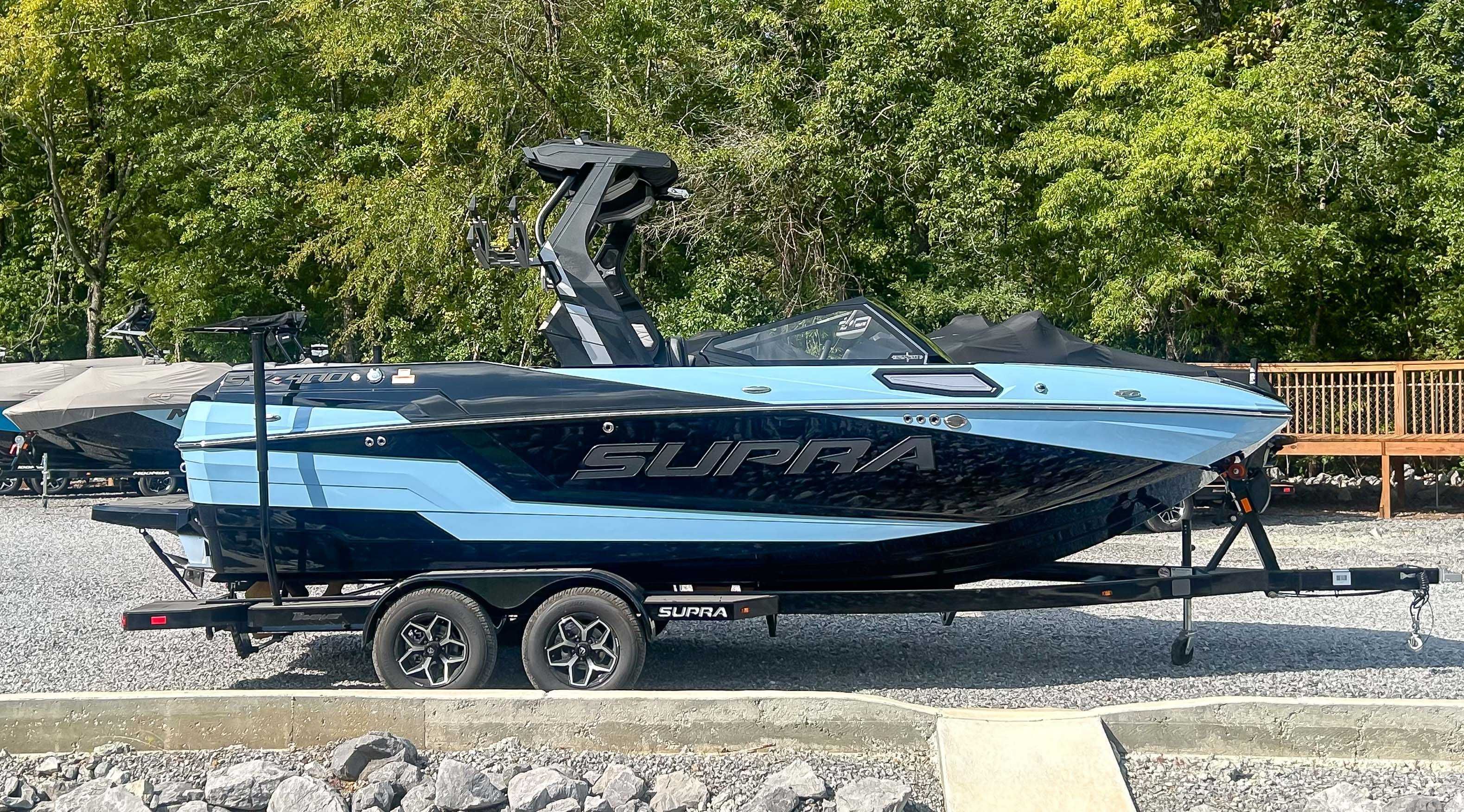 Supra SV 2025 Supra SV boat on trailer, parked outdoors with lush green background.