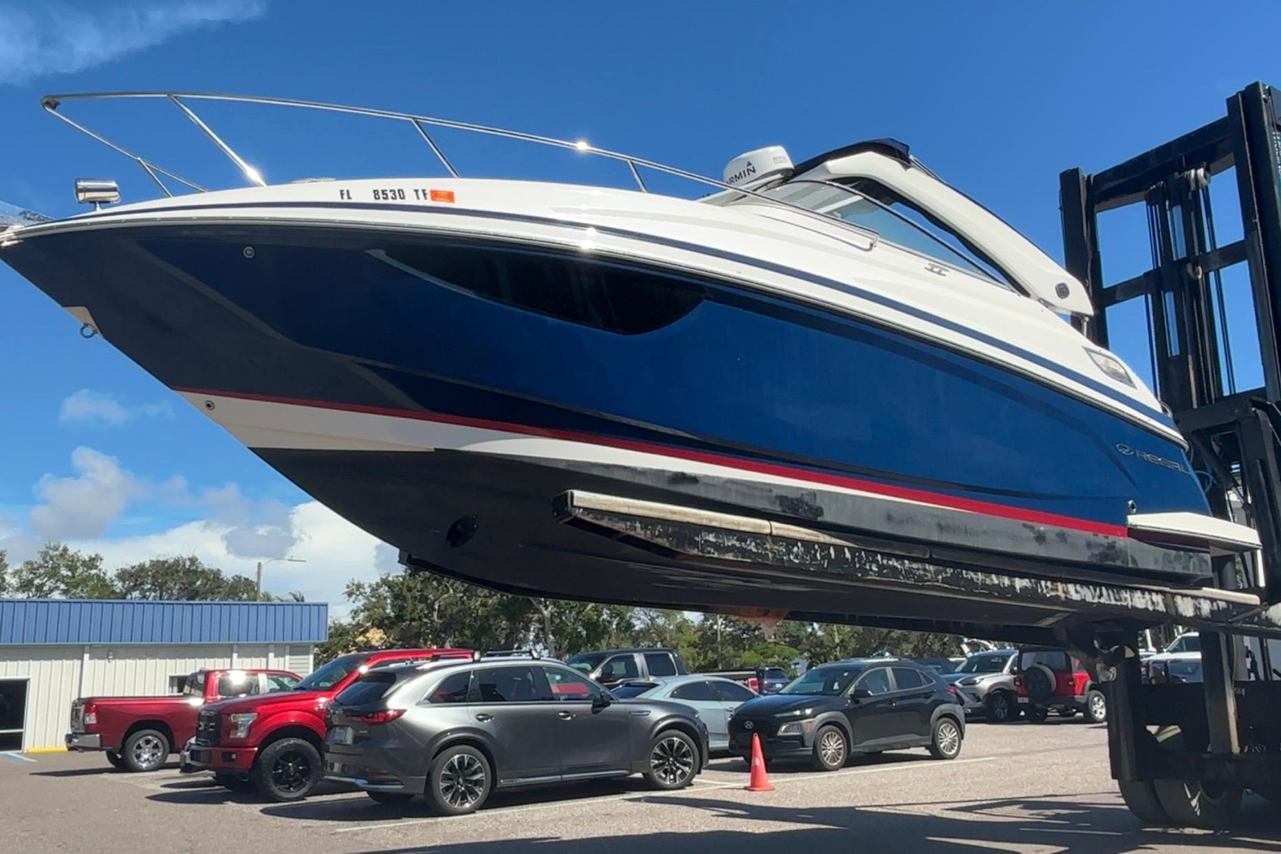 Regal 28 Express 2020 Regal 28 Express boat lifted, blue hull, parked cars in background.