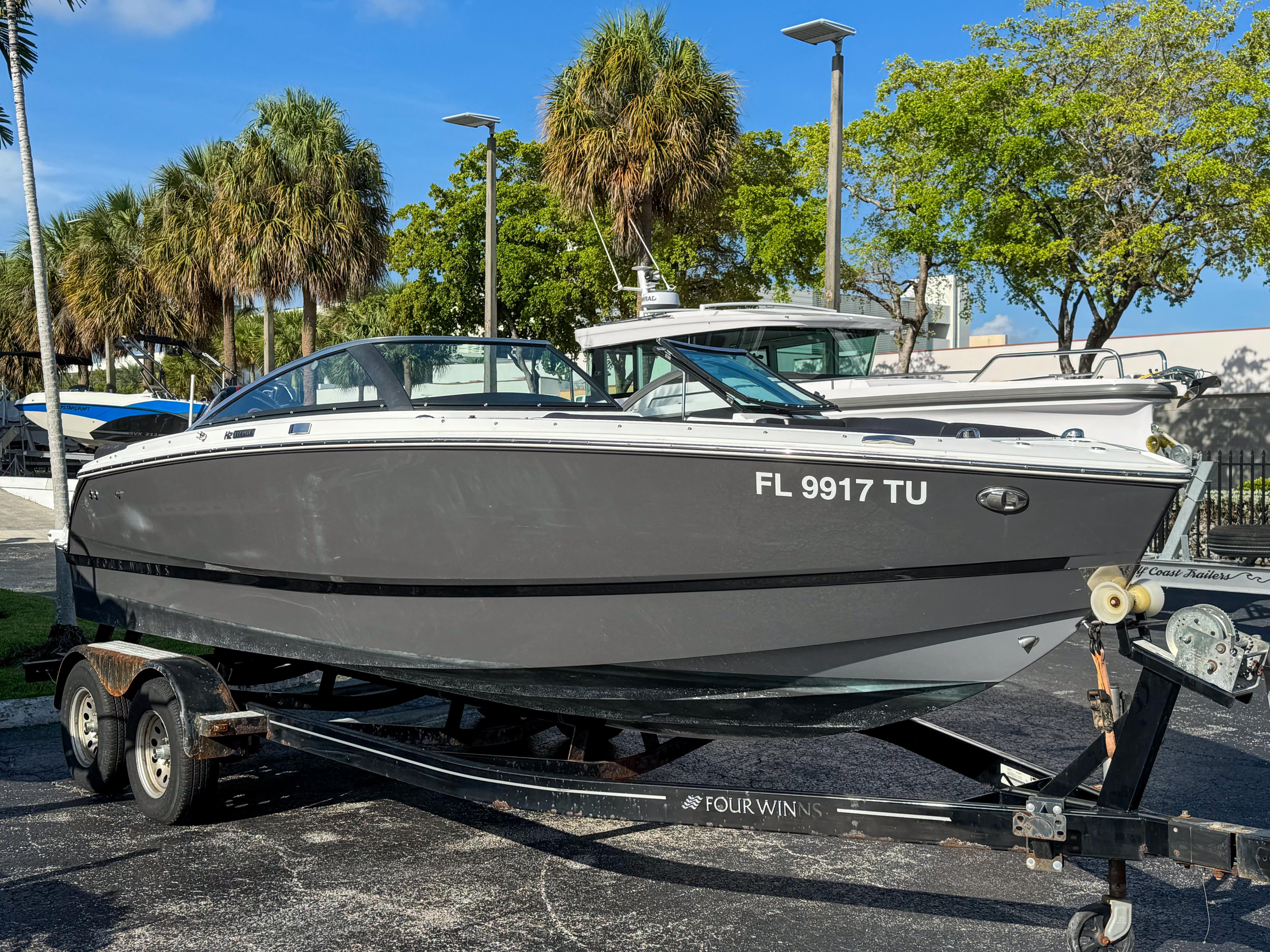 Four Winns H2 2021 Four Winns H2 boat on trailer, parked outdoors with palm trees in background.