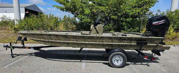 Tracker Grizzly 1860 CC 2025 Tracker Grizzly 1860 CC boat on trailer, parked outdoors, with Mercury outboard motor.