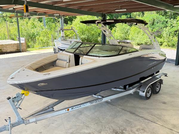 Regal LS6 Surf 2023 Regal LS6 Surf boat on trailer in covered area, surrounded by greenery.