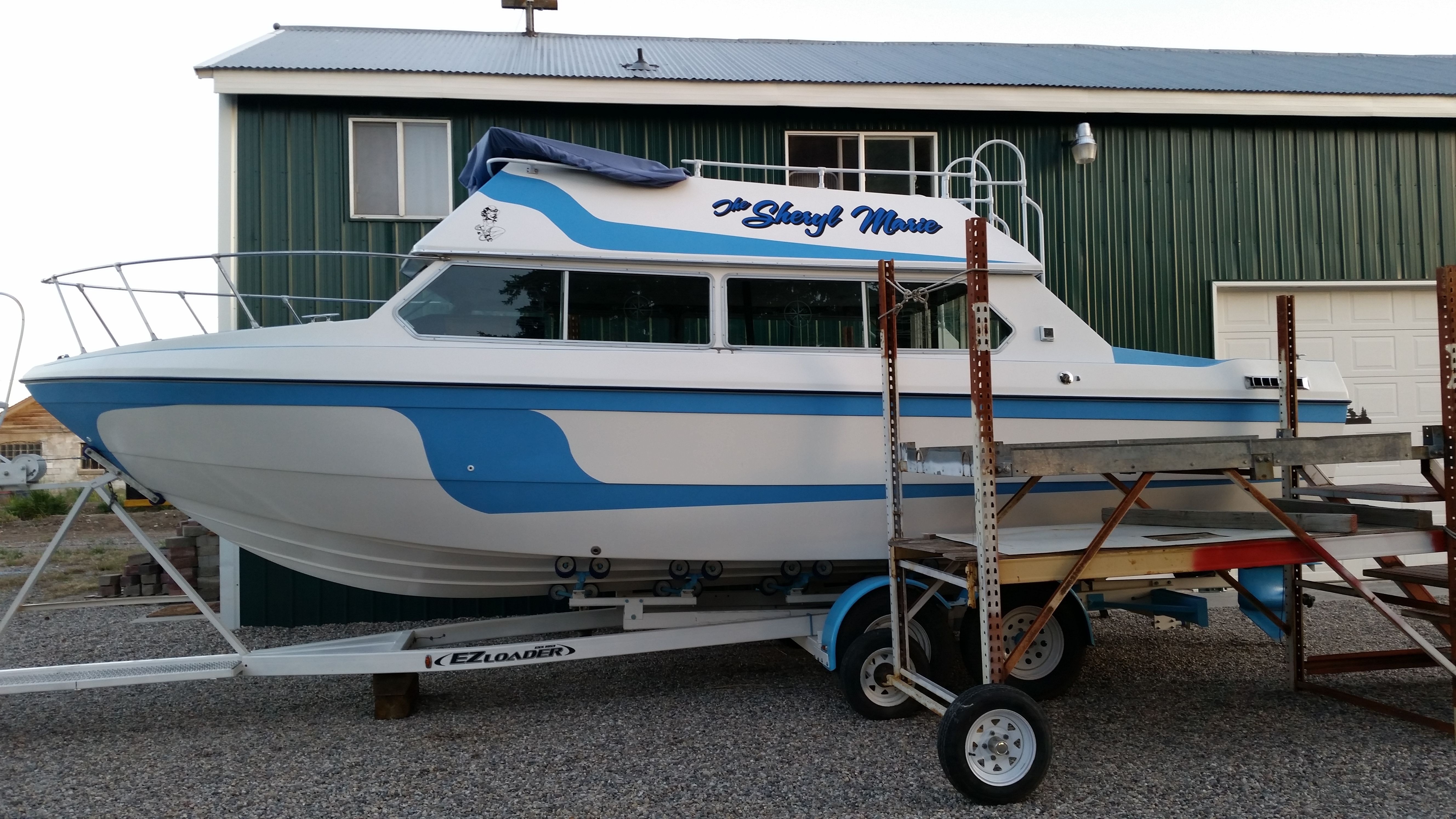 Apollo Voyager 1978 Apollo Voyager boat on trailer, blue and white design, parked outside green building.