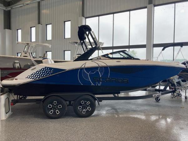 Scarab 215 2023 Scarab 215 boat in showroom, blue and white design, on a trailer.