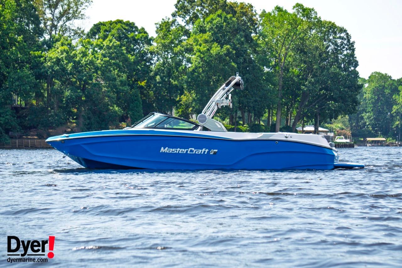 MasterCraft XT24 2024 MasterCraft XT24 boat on a lake with lush green trees in the background.