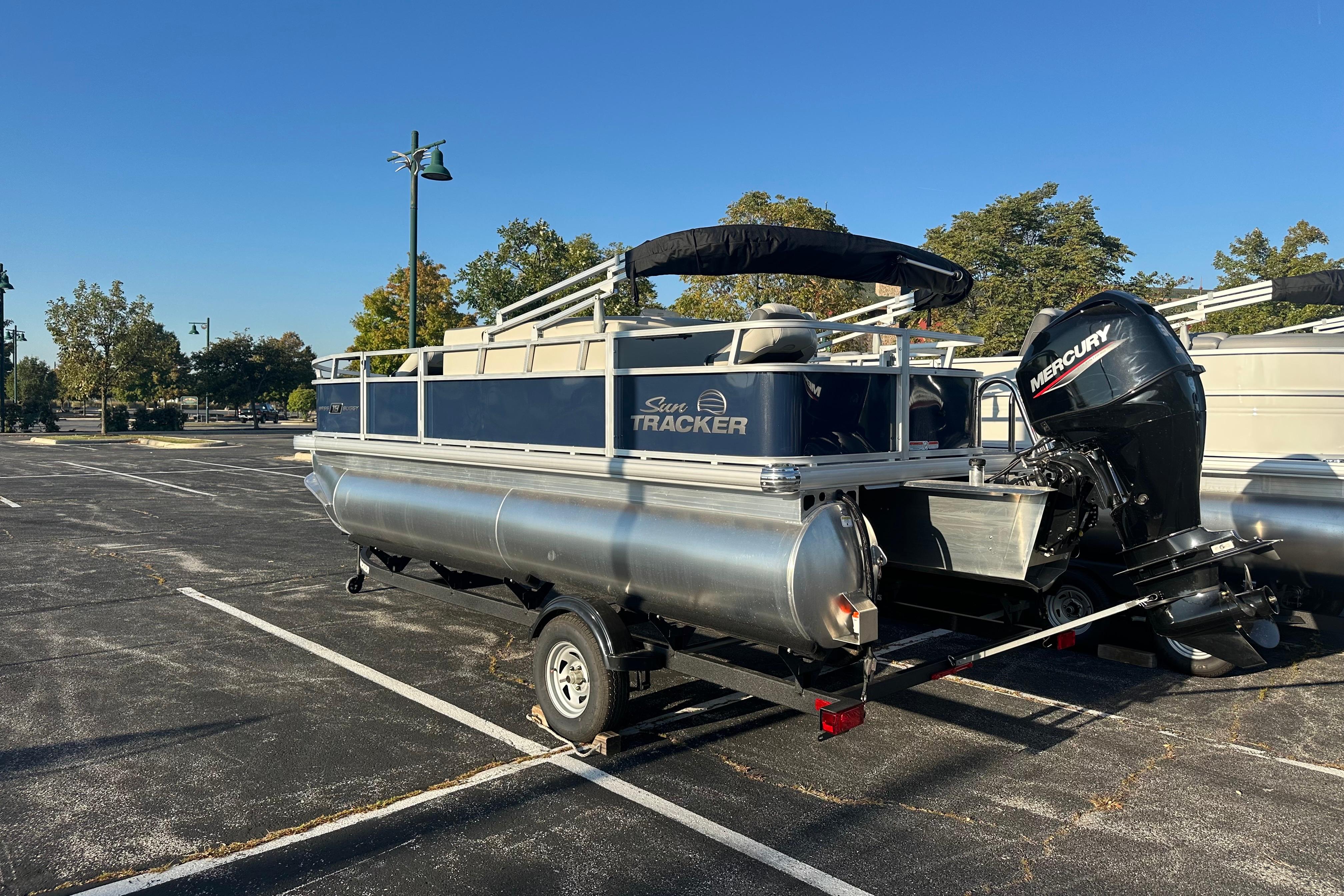 Sun Tracker Bass Buggy 18 DLX 2026 Sun Tracker Bass Buggy 18 DLX pontoon boat on trailer in parking lot.