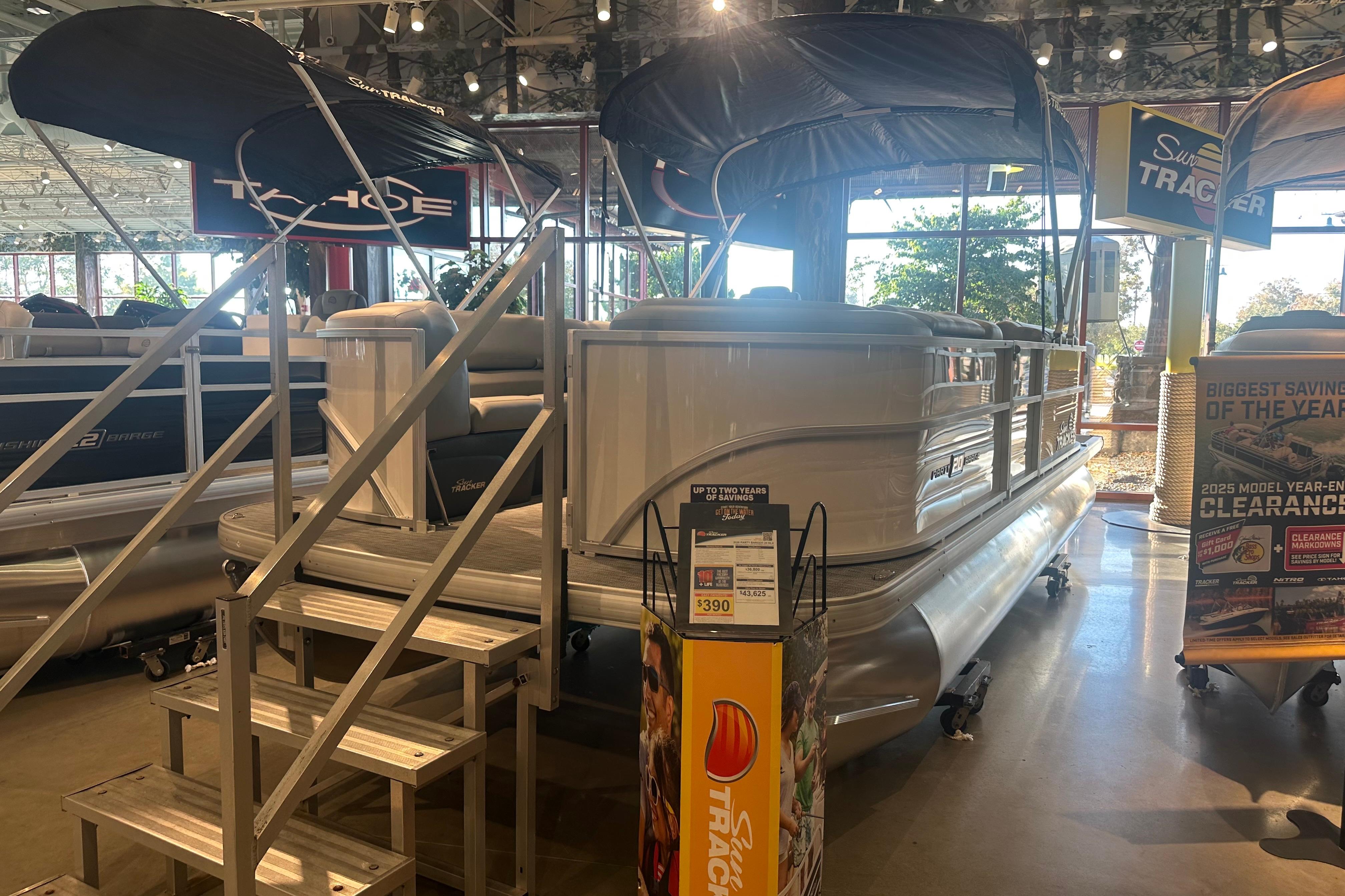 Sun Tracker Party Barge 20 DLX 2026 Sun Tracker Party Barge 20 DLX pontoon boat displayed indoors with promotional signage.