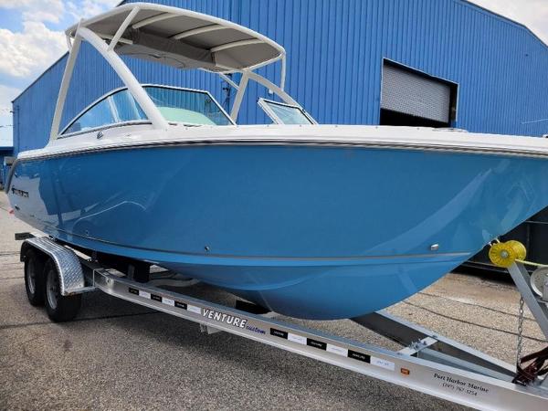 Sailfish 236 DC 2025 Sailfish 236 DC boat on a Venture trailer, blue hull, parked outside a blue building.
