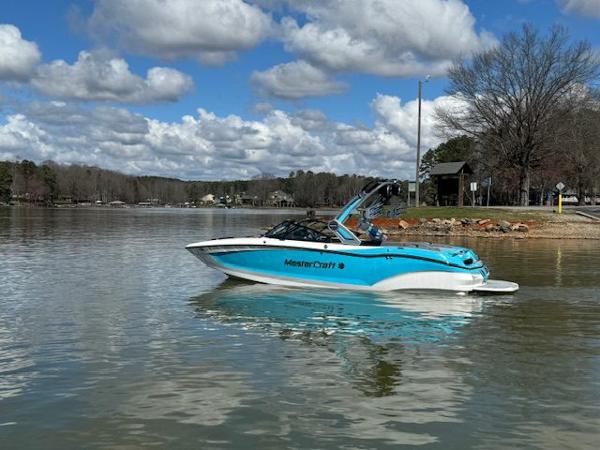 MasterCraft X22 2024 MasterCraft X22 boat on a serene lake under a cloudy sky.