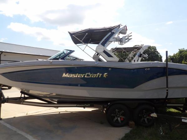 MasterCraft X24 2024 MasterCraft X24 boat on trailer, blue and gray design, parked outdoors.