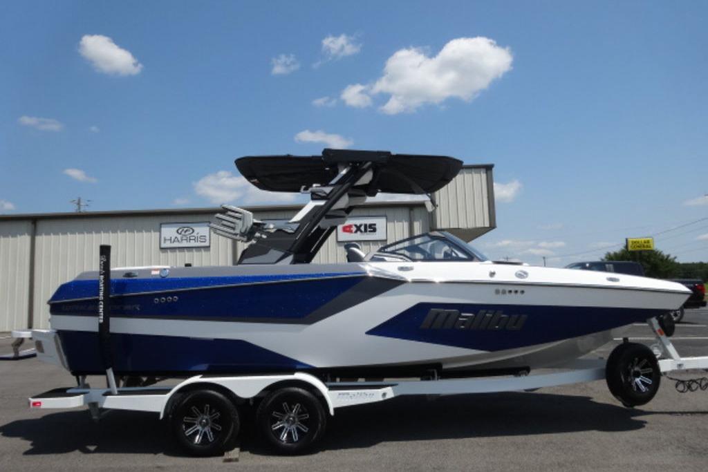 Malibu 23 MXZ 2026 Malibu 23 MXZ boat on trailer, blue and white design, parked outdoors.