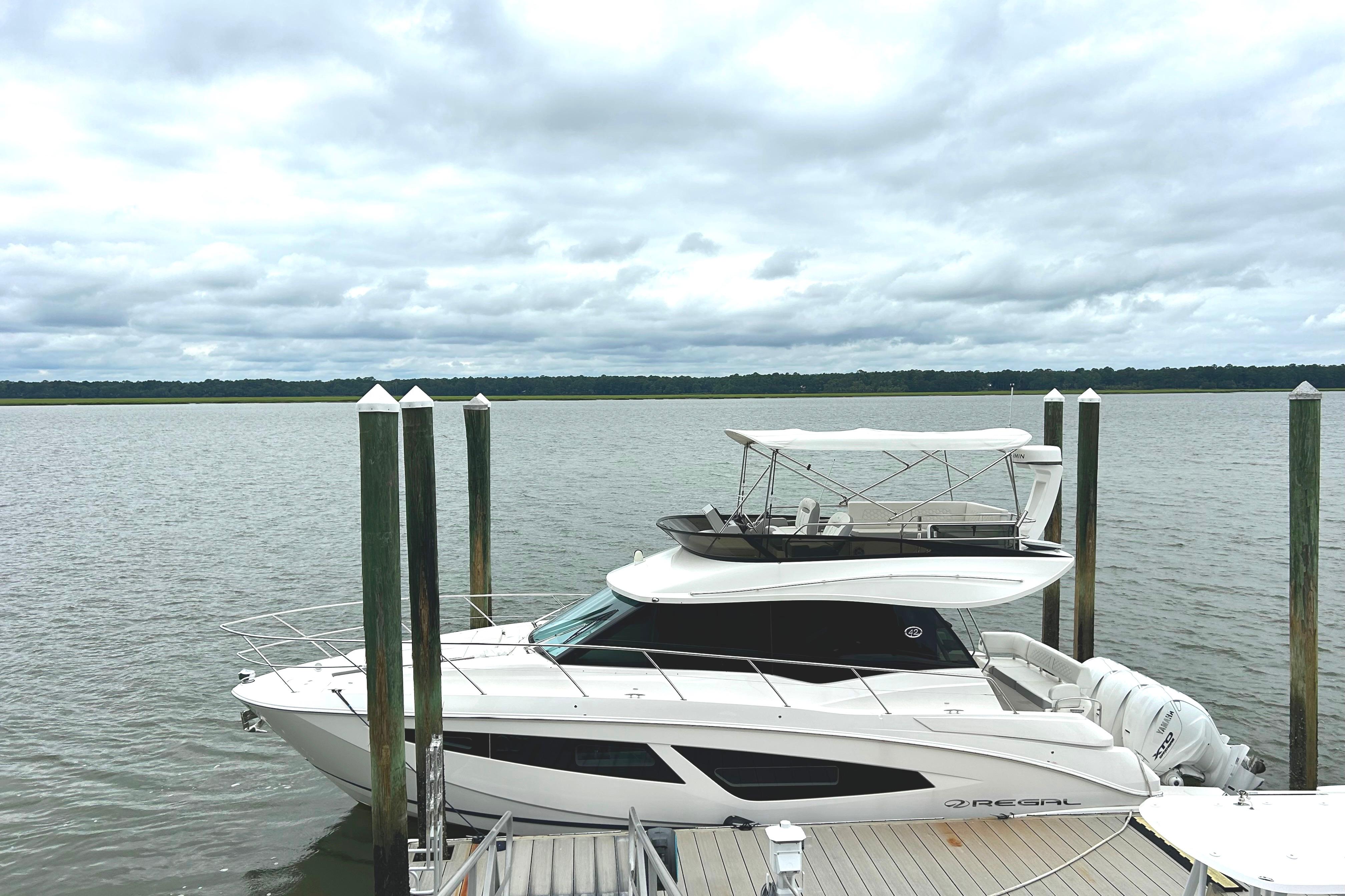 Regal 42 FXO 2024 Regal 42 FXO yacht docked by a serene waterfront under cloudy skies.