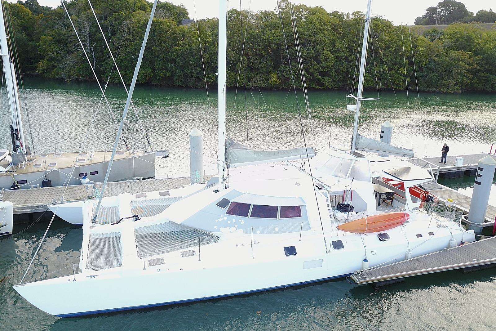 Custom CATAMARAN CUSTOM 60' Custom 60' catamaran from 1996 docked by a lush, green shoreline.