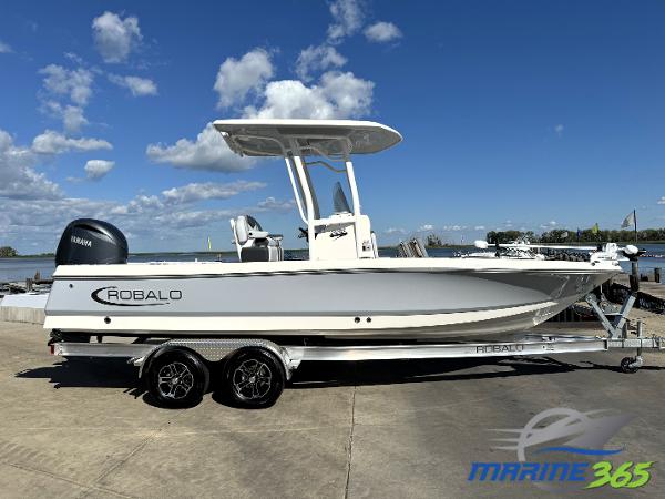 Robalo 226 Cayman 2025 Robalo 226 Cayman boat on trailer, parked by waterfront under blue sky.