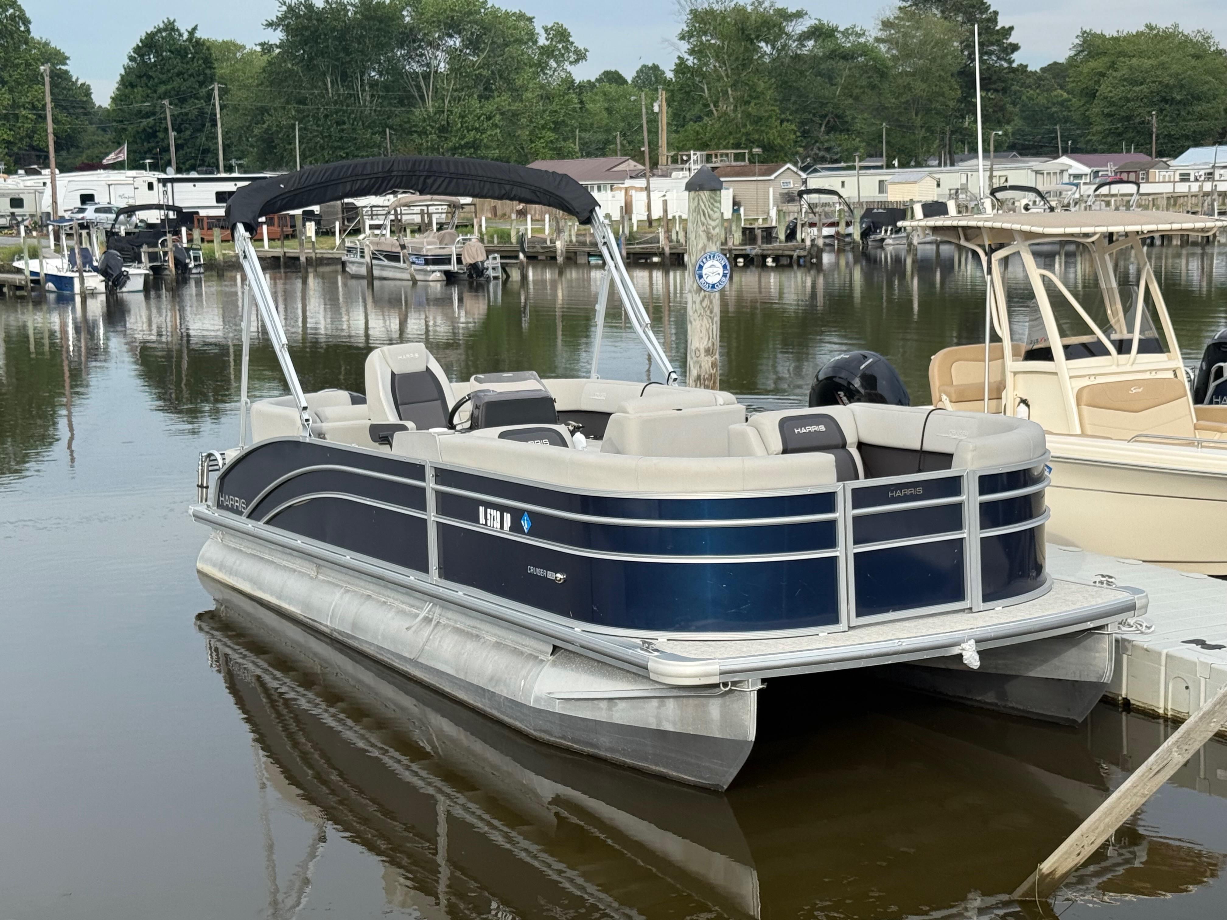 Harris Cruiser 230 2024 Harris Cruiser 230 pontoon boat docked at a marina, surrounded by calm water.
