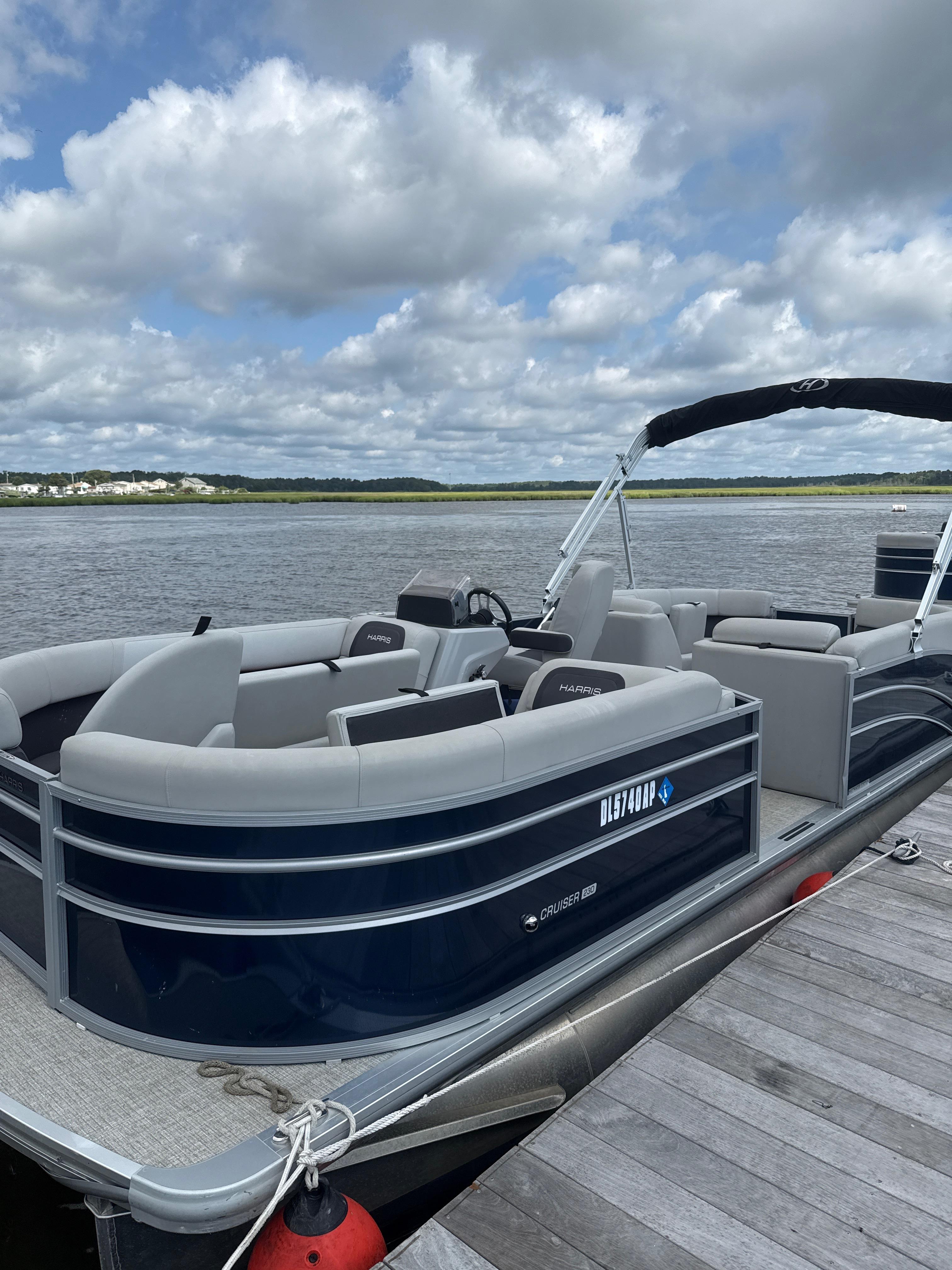 Harris Cruiser 230 2024 Harris Cruiser 230 pontoon boat docked on a calm lake under a cloudy sky.