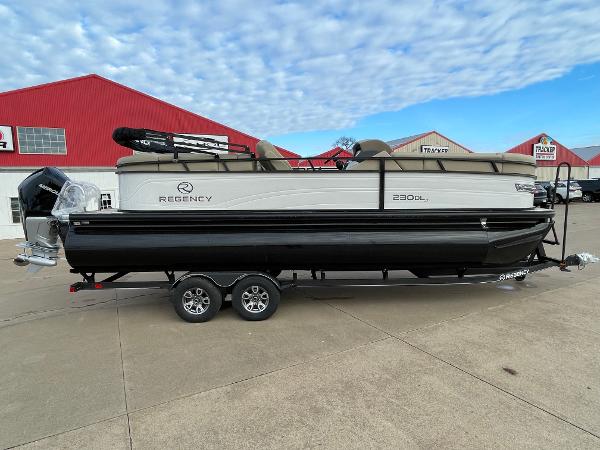 Regency 230 DL3 2024 Regency 230 DL3 pontoon boat on a trailer, parked outside a dealership.
