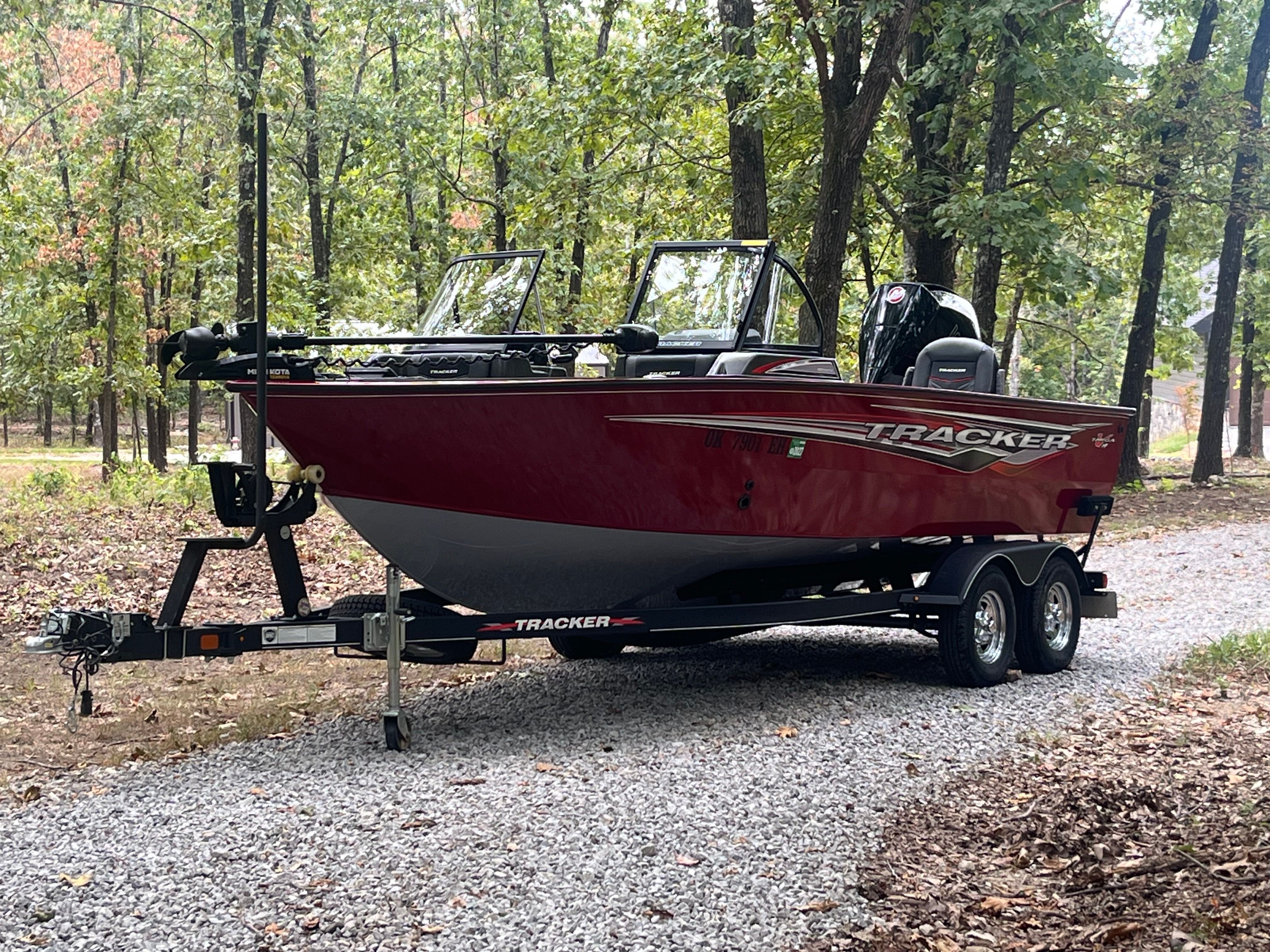 Tracker targ Red 2021 Tracker Targ boat on trailer in wooded area.