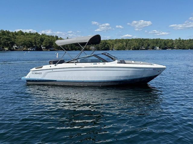 Cobalt R4 2025 Cobalt R4 boat on a serene lake with a canopy under a clear blue sky.