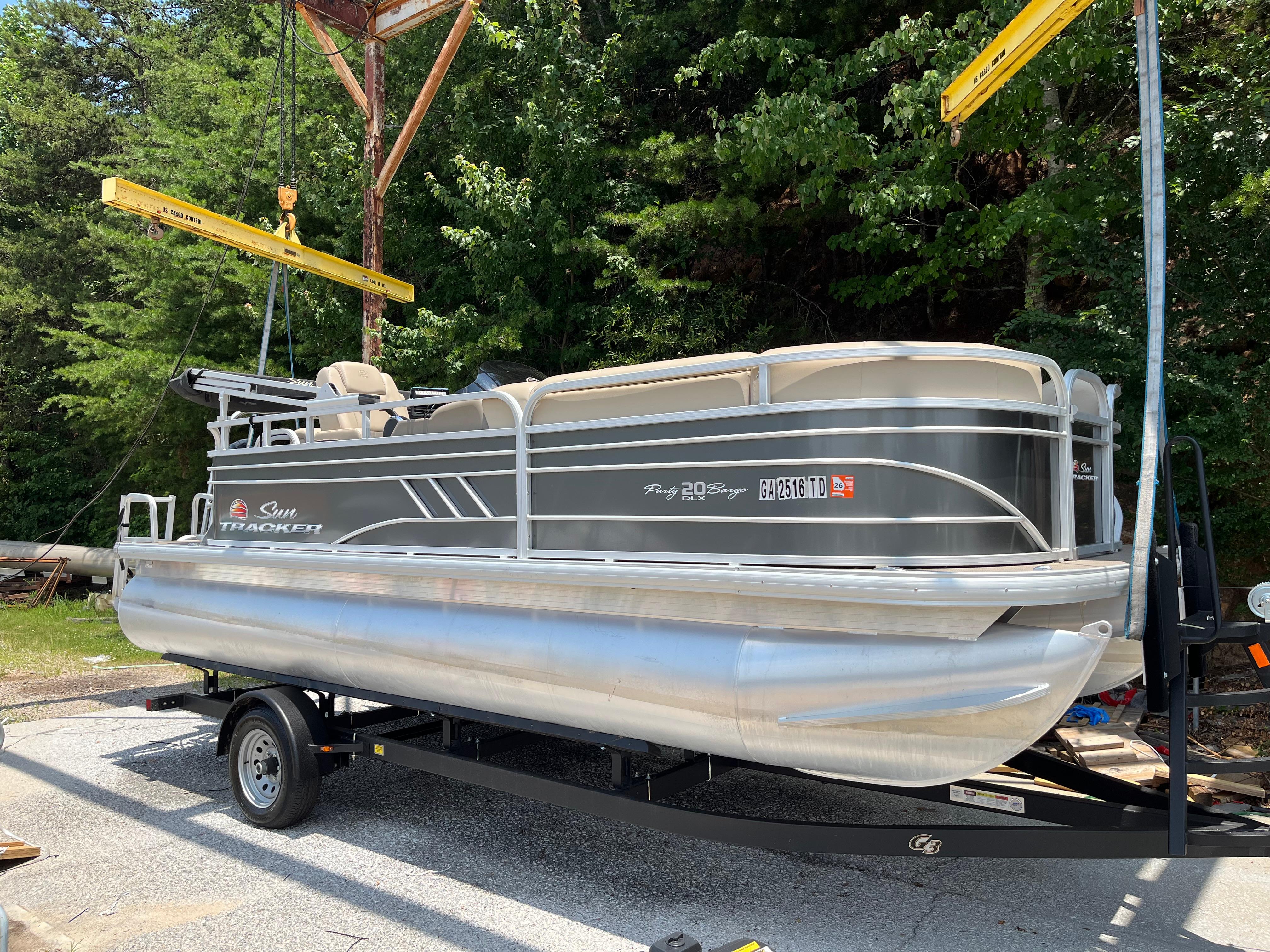 Sun Tracker Party Barge 20 DLX 2022 Sun Tracker Party Barge 20 DLX pontoon boat on trailer, surrounded by trees.