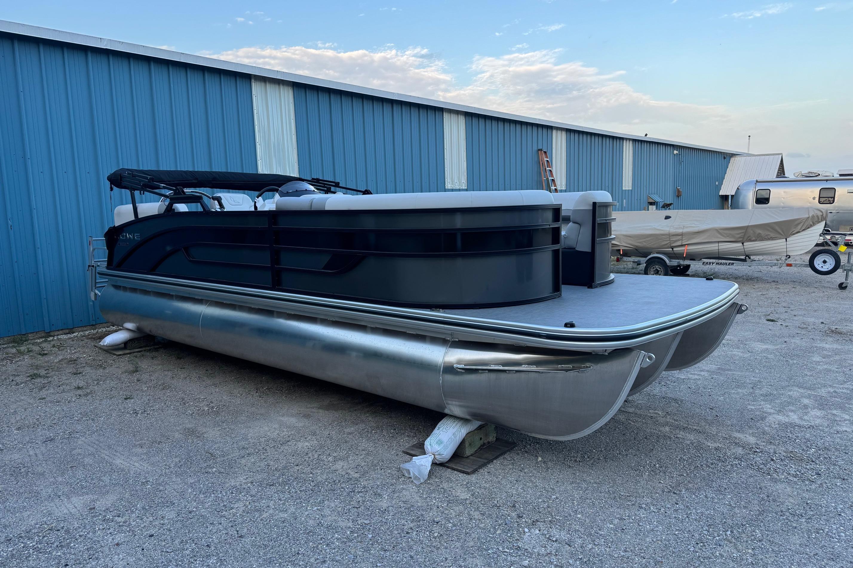 Lowe SS230WV 2025 Lowe SS230WV pontoon boat parked beside a blue warehouse.