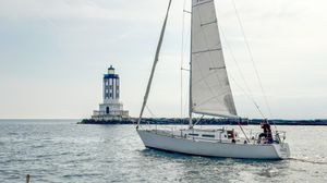 Sailboat Racing Sloop Sailboat Racing Sloop 1983 near lighthouse on calm sea.
