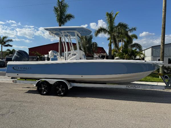 Robalo 246 Cayman 2023 Robalo 246 Cayman boat on trailer, parked near palm trees under a clear sky.