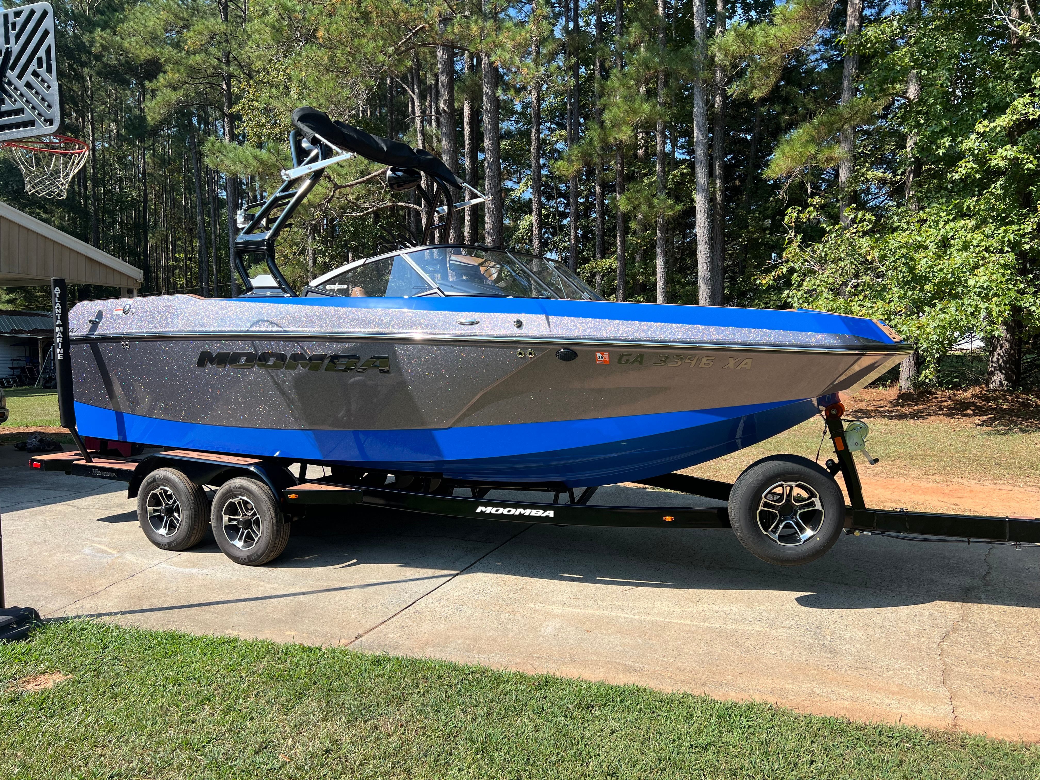 Moomba Max 2023 Moomba Max boat on trailer, parked in driveway, surrounded by trees.