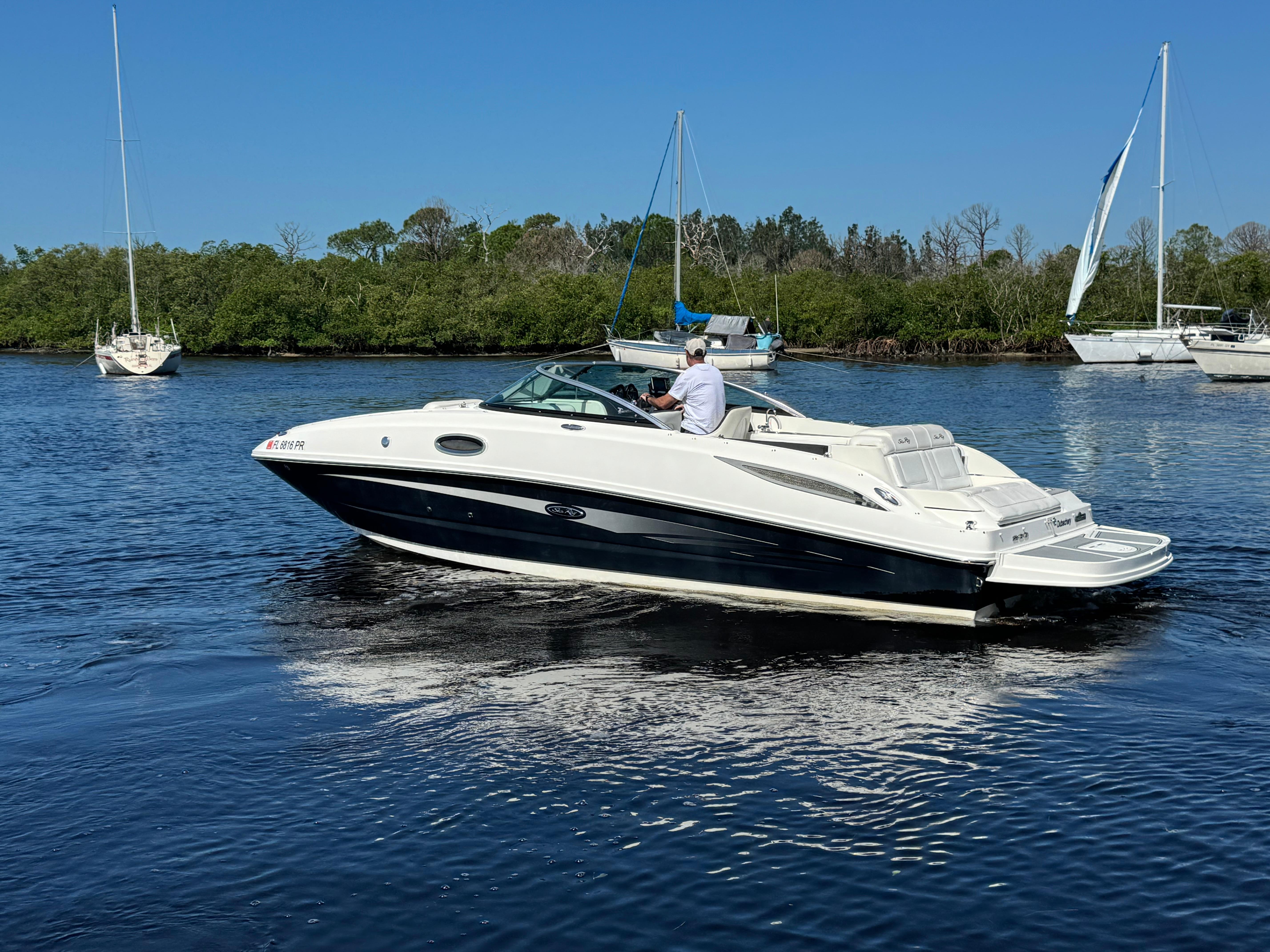 Sea Ray 260 Sundeck 2014 Sea Ray 260 Sundeck cruising on a calm river with sailboats in the background.
